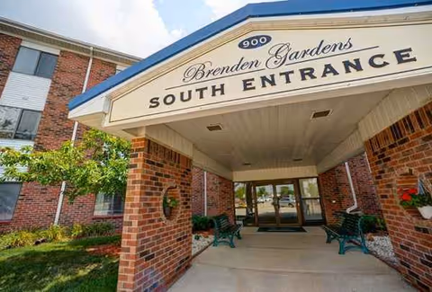 Brick senior living facility entrance with a covered walkway and benches.