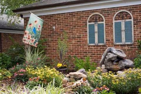 Exterior of a brick senior living facility with a colorful garden and rock fountain.