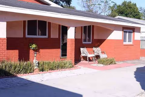 Front exterior of a red-brick senior living facility with porch seating.