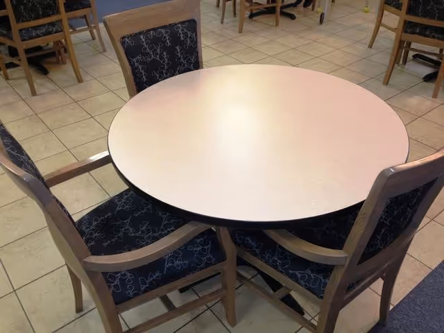 Round dining table with four wooden chairs that have dark patterned cushions, set on a tiled floor in a dining area.