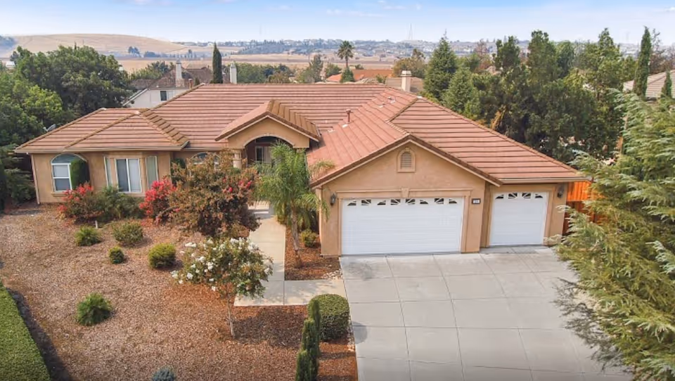 Single-story stucco home with a three-car garage, tile roof, driveway, and landscaped front yard.