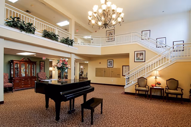 Spacious lobby atrium with a black grand piano, seating areas, a chandelier, and a staircase leading to an upper balcony.