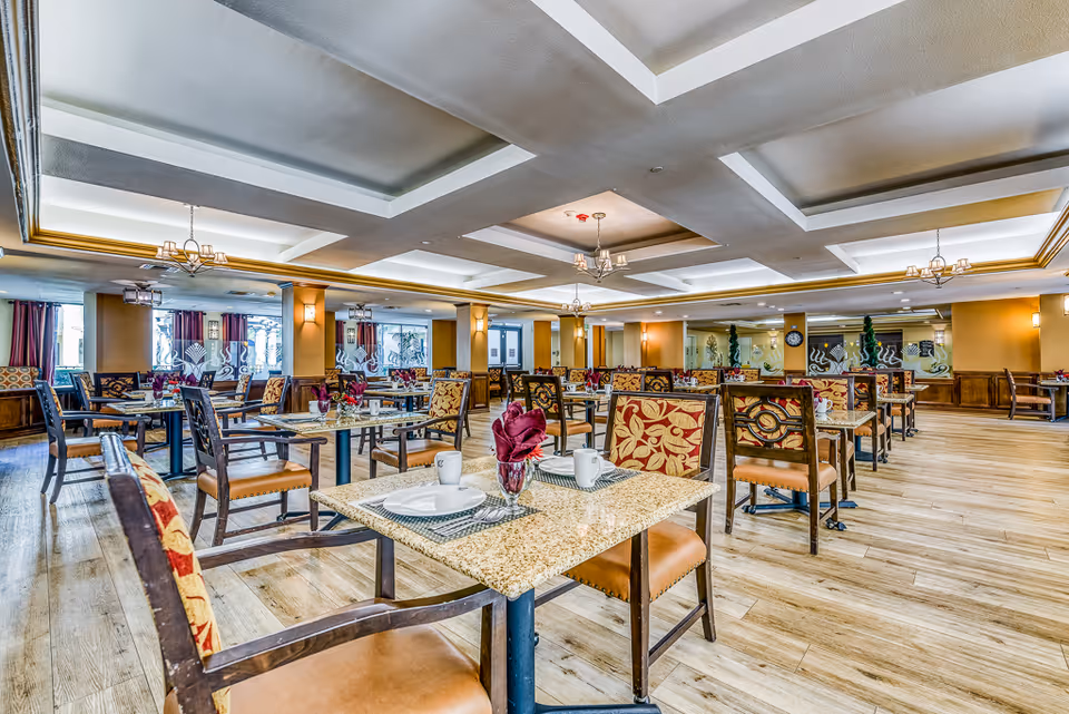Spacious dining room with multiple set tables and patterned chairs under coffered ceilings and chandeliers.