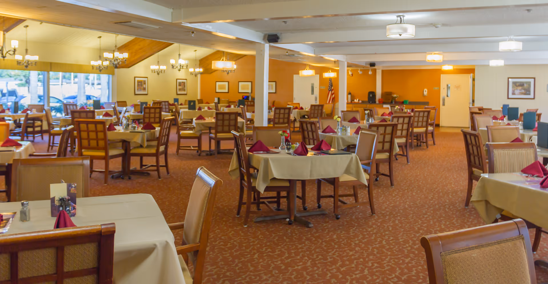 Spacious dining room with multiple tables covered in tablecloths and set with folded napkins and centerpieces.