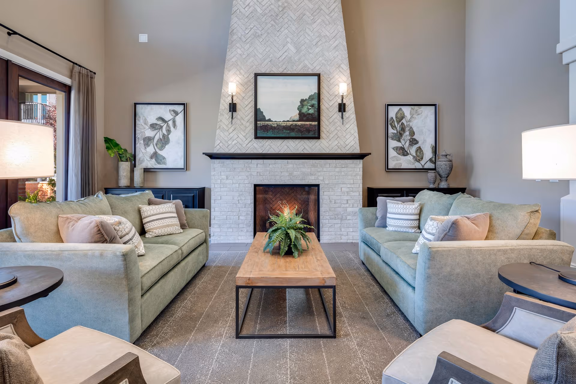 Bright modern living room with two green sofas facing a central fireplace, a wooden coffee table, and decorative wall art.
