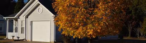 Front exterior of Maples at Austin Place with a garage and autumn tree