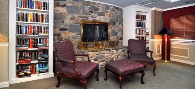 Cozy sitting area with a stone fireplace flanked by built-in bookshelves and two upholstered chairs with an ottoman.