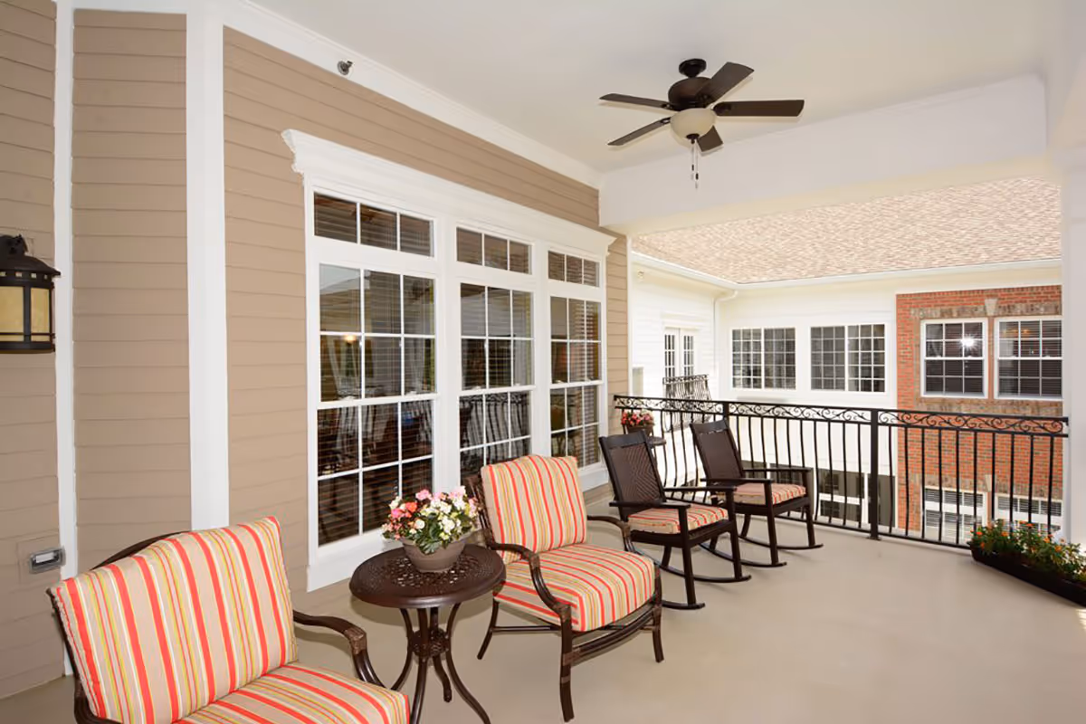 A cozy patio area featuring striped chairs and a small table, with large windows in the background and a decorative railing.