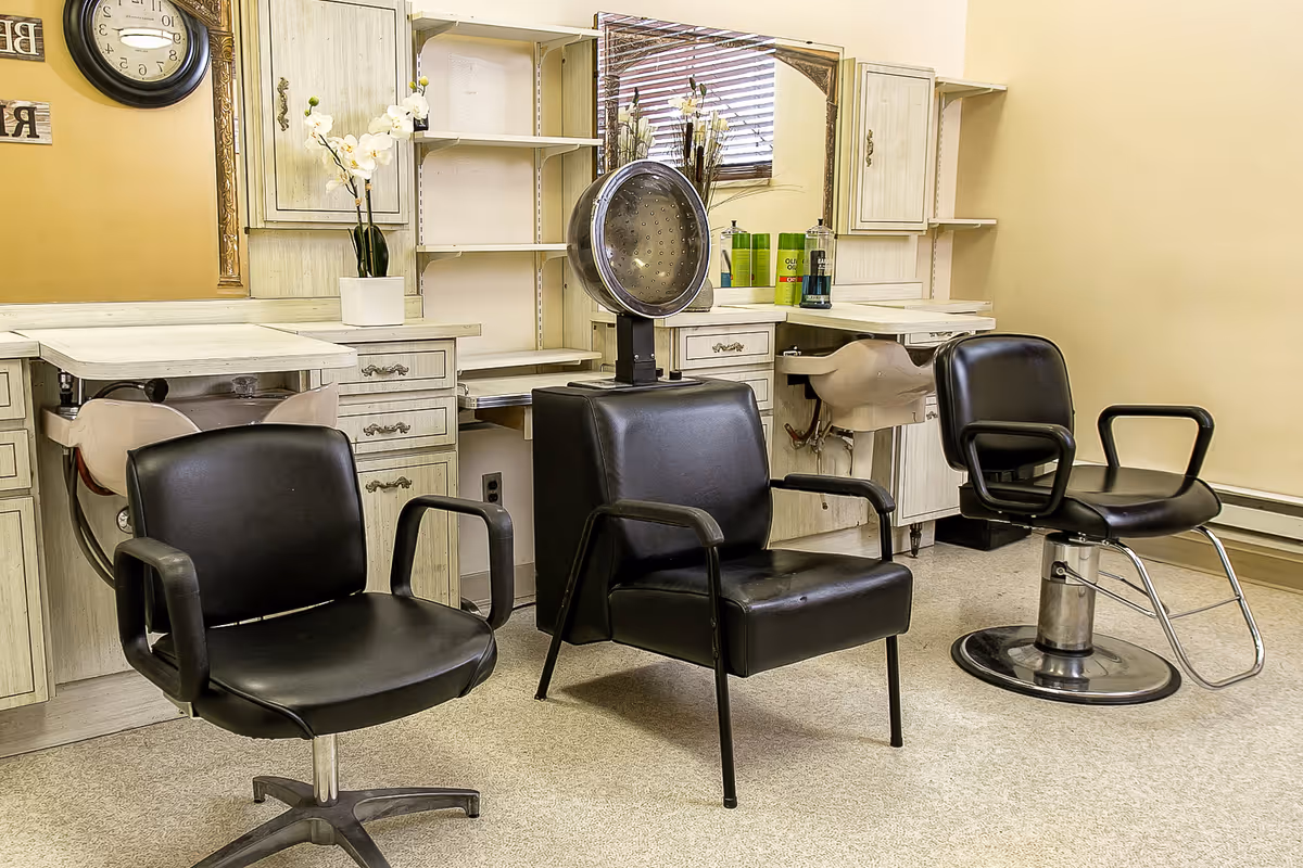 Interior salon area with three black styling chairs, a hooded hair dryer, and counter stations with mirrors.