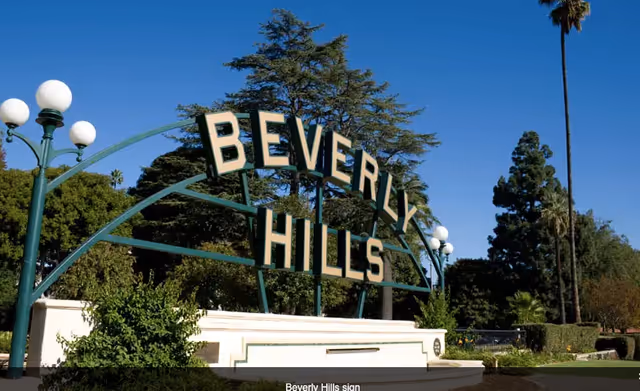 Green metal arch reading 'Beverly Hills' in a landscaped park under a clear blue sky.