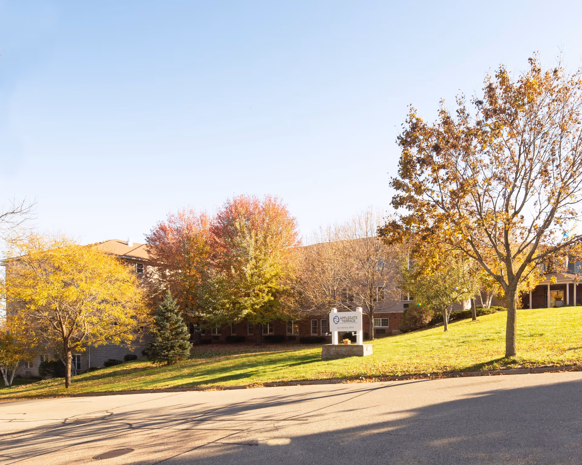 Applegate Terrace senior living building on a grassy hill, surrounded by autumn trees with a sign at the front.