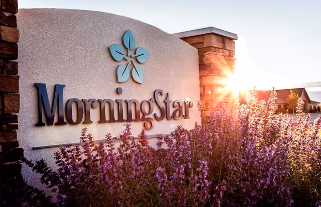 Sunlit stone entrance sign reading "MorningStar" with purple flowers in the foreground and the sun rising behind it.