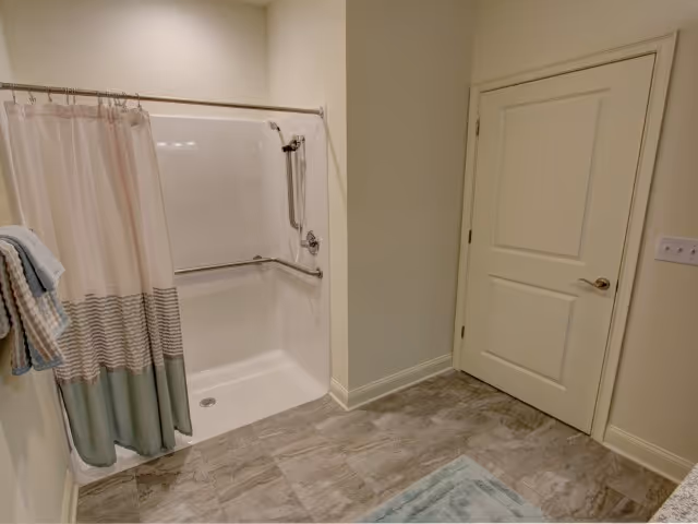 Accessible bathroom featuring a walk-in shower with grab bars and a shower curtain, tiled floor, and a closed door.