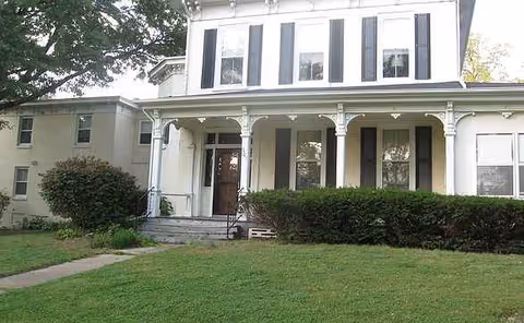 Front view of a two-story white building with a covered porch and green lawn.