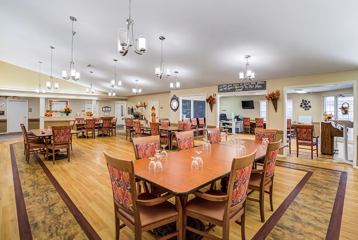 Bright communal dining room with multiple wooden tables and patterned chairs arranged under pendant lights.