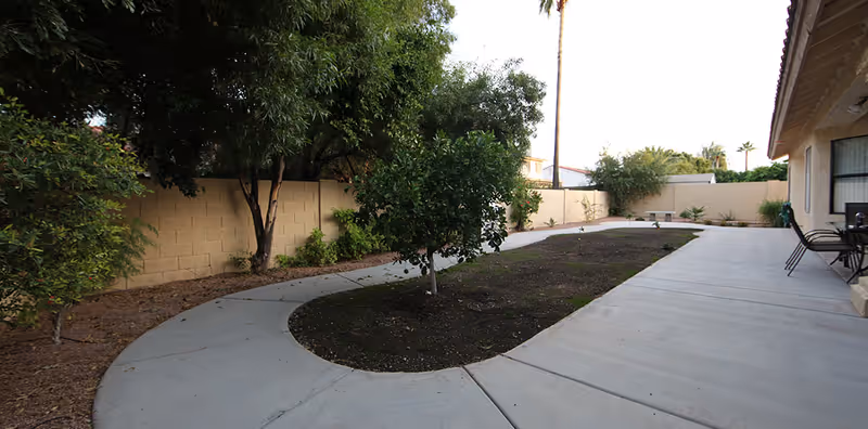 Outdoor courtyard with curved walkway, trees, and patio seating beside a beige building.
