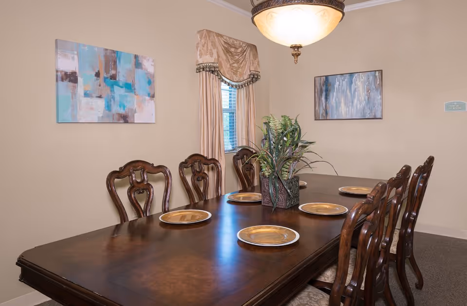 Wood dining table with six ornate chairs, place settings and a potted centerpiece in a decorated dining room.