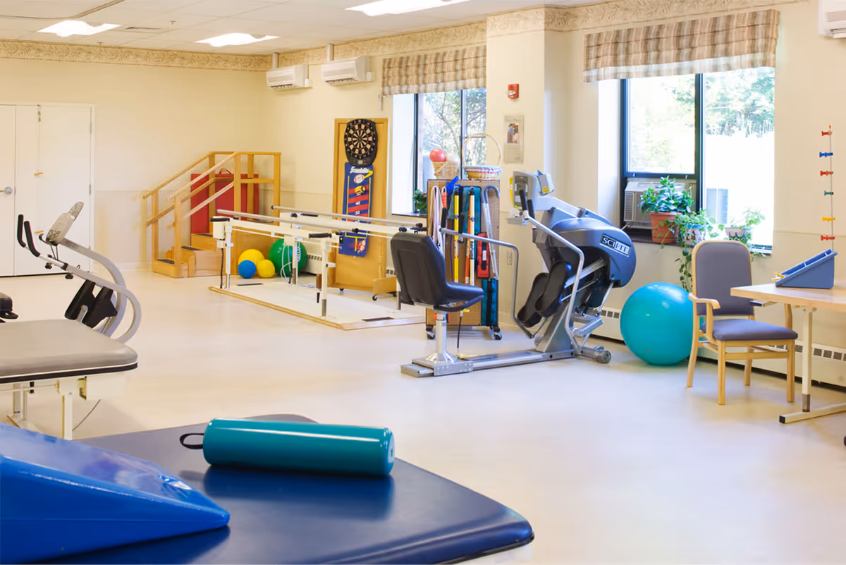 Bright rehabilitation/exercise room with parallel bars, exercise machines, therapy balls and chairs.