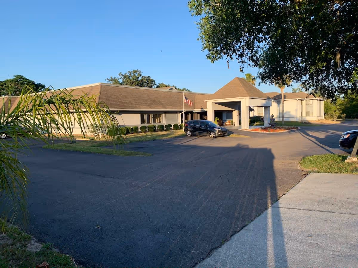 Exterior view of Oakview Terrace Assisted Living and Memory Care building with a driveway and parked cars under a clear blue sky, surrounded by trees and landscaping.