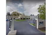 Exterior view of Bryn Mawr Extended Care Center entrance with gate, driveway, and surrounding trees.