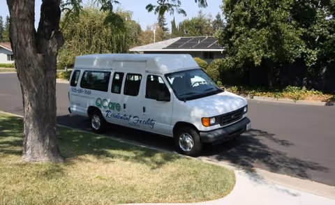 White van with Qcare Residential Facility logo parked on a suburban street near trees