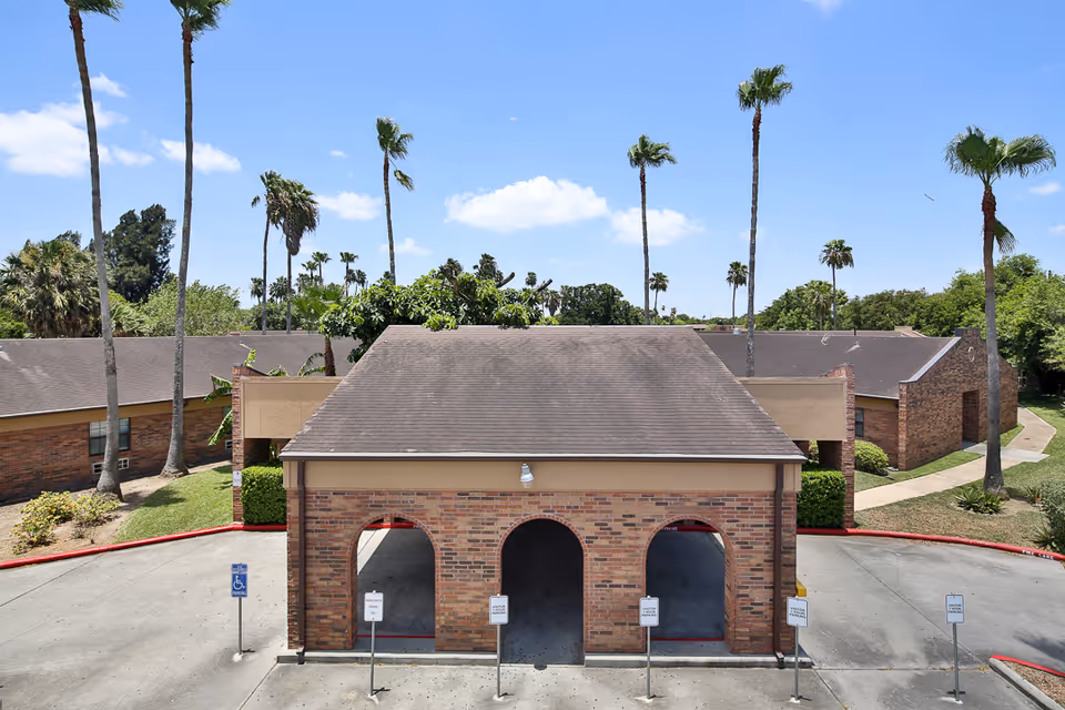 Brick portico with three arched openings at the front of a nursing facility, surrounded by parking and tall palm trees.