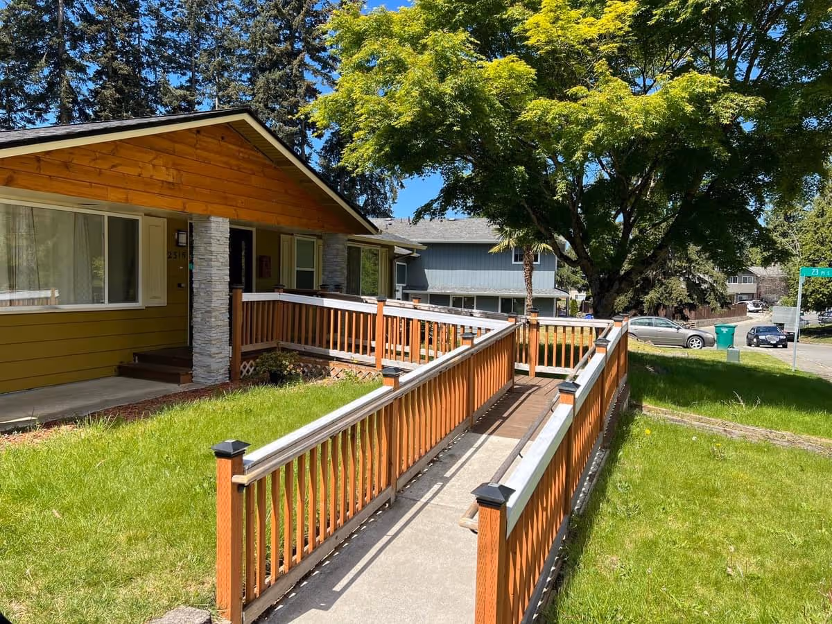 Front exterior of a yellow single-story home with ramp and wooden railing