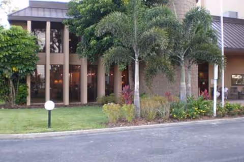 Exterior view of River Commons facility with glass doors, landscaping, and palm trees.