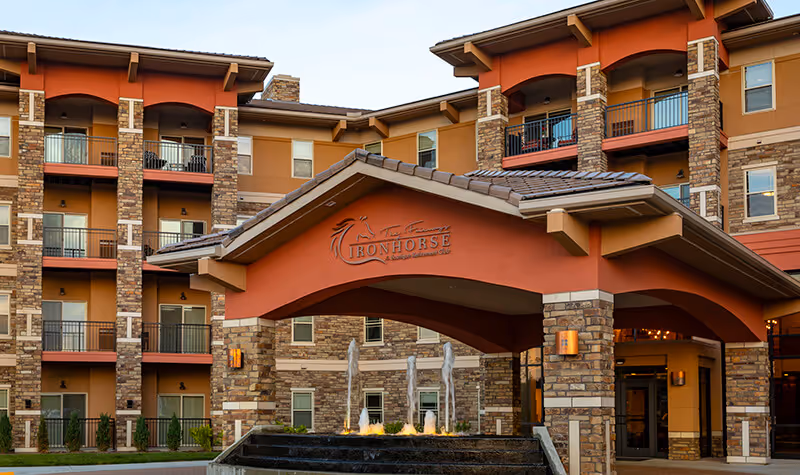 Front entrance of Fairways of Ironhorse independent living with a covered porte-cochere, stone facade, balconies and a fountain.