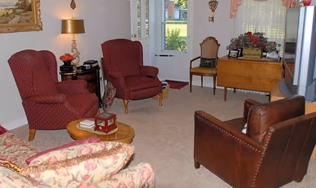 Cozy living room with patterned armchairs, a leather chair, a floral sofa, small tables, and a doorway leading outside.