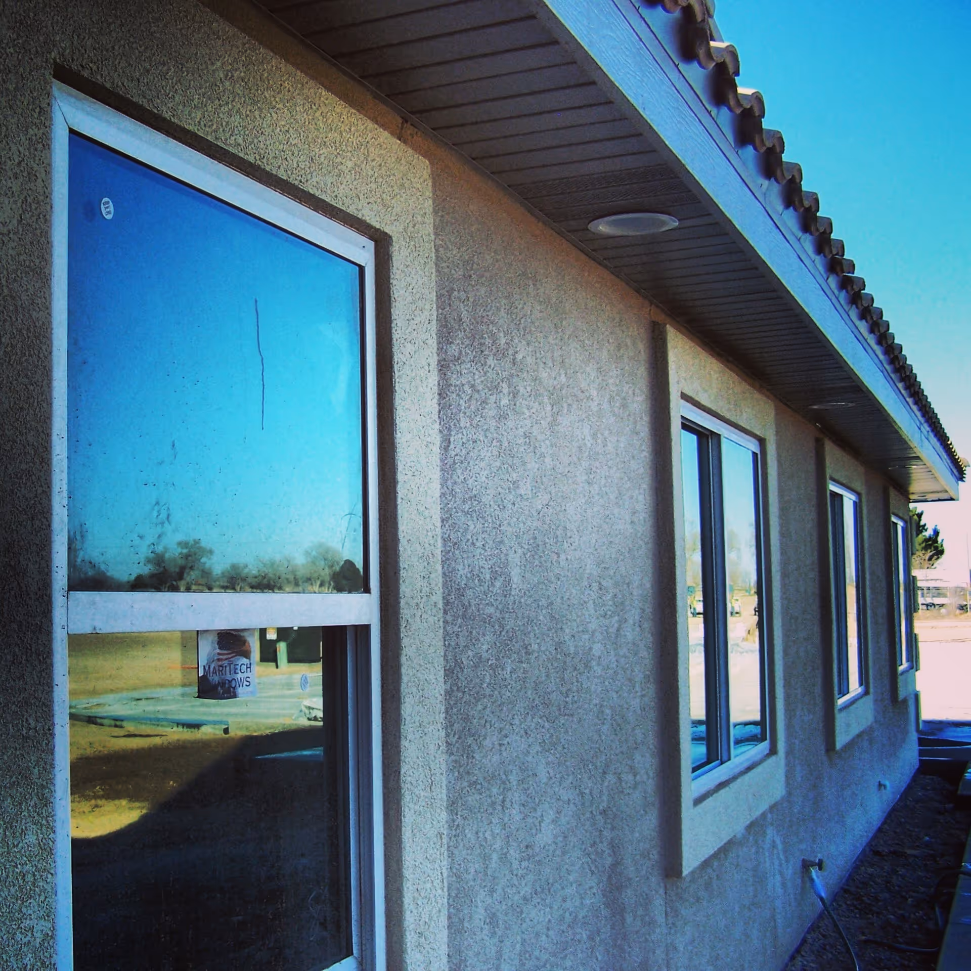 Exterior side view of a building wall with three windows and a tiled roof under a clear blue sky.