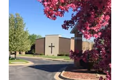 Front exterior of Davenport Lutheran Home with a cross, pink flowering tree, and parking lot.