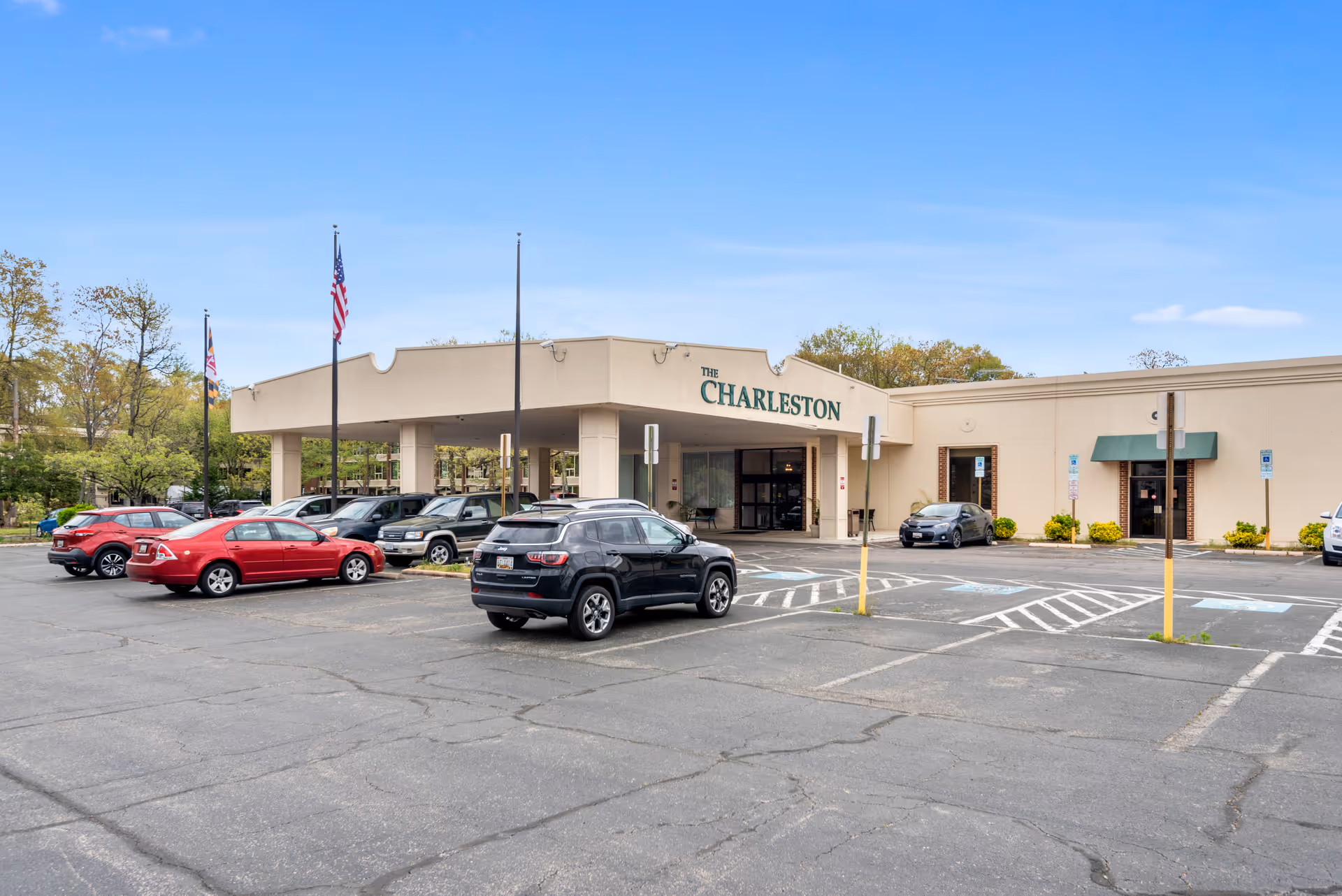 Parking lot and main entrance of The Charleston Senior Community building with cars, flagpoles, and accessible parking spaces.