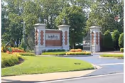Entrance sign for AdamsPlace facility with brick and stone pillars, surrounded by landscaped greenery and trees in the background.