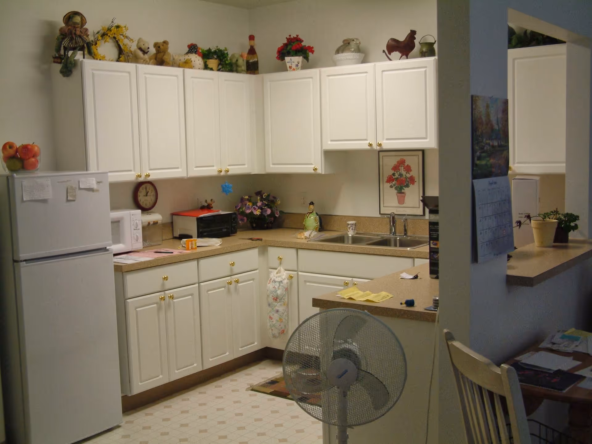 Small apartment kitchen with white cabinets, a refrigerator, sink, countertop appliances and decorative items.