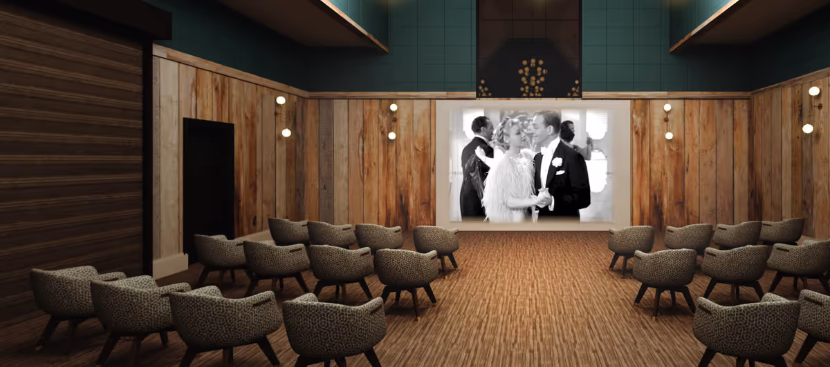 Small screening room with rows of upholstered chairs facing a screen showing a black-and-white film, wood-paneled walls and warm lighting.