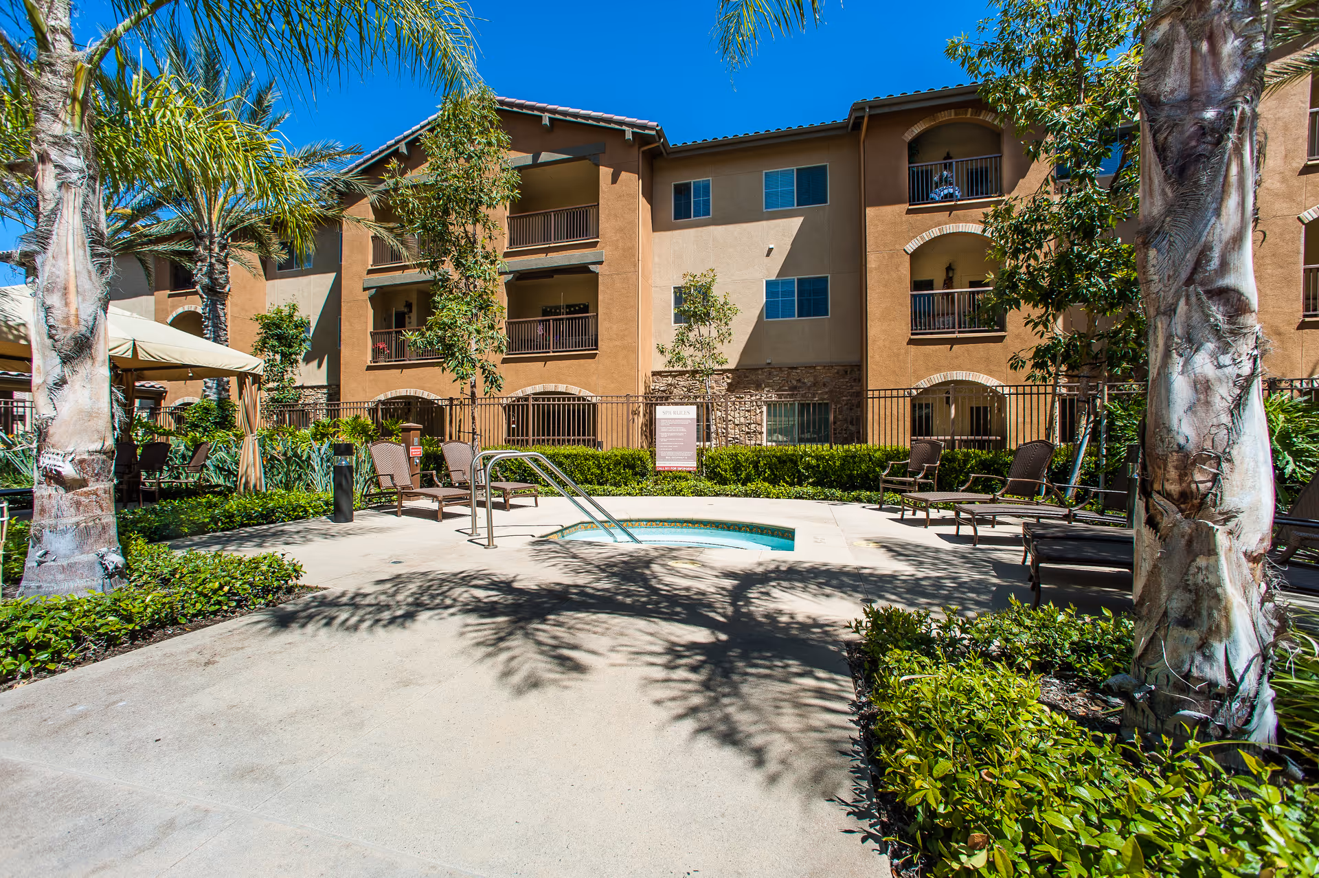 Outdoor courtyard area at Valencia Terrace featuring a small circular pool or hot tub surrounded by lounge chairs and palm trees, with a multi-story residential building in the background under a clear blue sky.