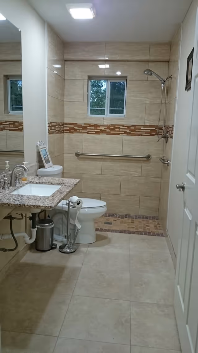 Tiled accessible bathroom with a walk-in shower, grab bar, toilet, and sink vanity.