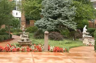 Outdoor garden courtyard at Rivermont Independent Living with statues, flowers, and paved paths.