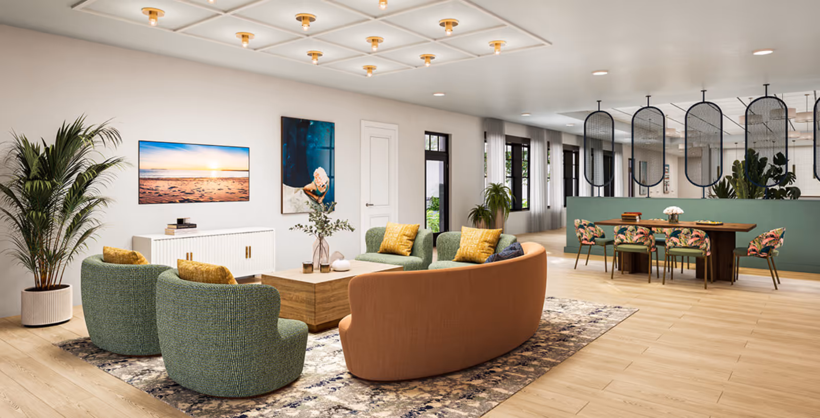A modern and spacious living room area with a curved orange sofa, two green armchairs with yellow pillows, and a wooden coffee table on a patterned rug. The room features light wood flooring, large potted plants, wall art including a beach sunset photo, and a dining area with a wooden table and six floral-patterned chairs separated by decorative black mesh panels.