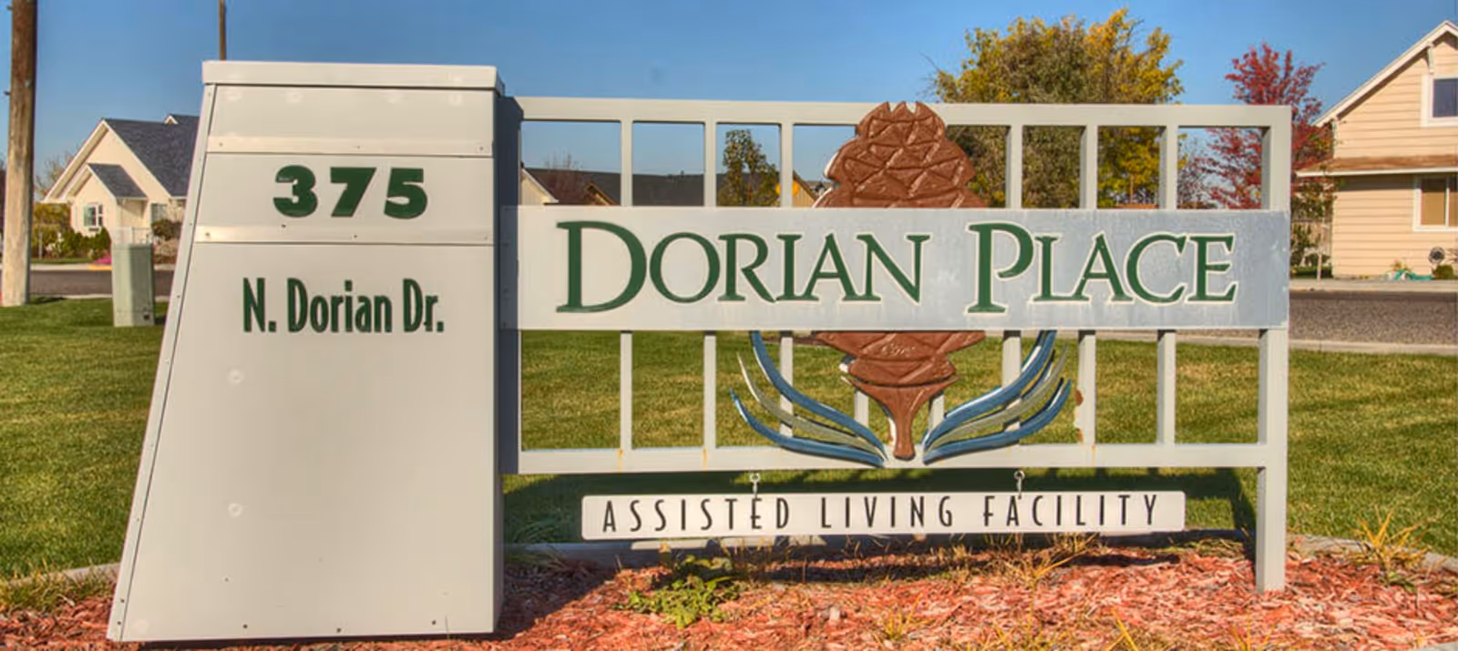 Outdoor sign for Dorian Place Assisted Living Facility located at 375 N. Dorian Dr., with houses and green lawns in the background under a clear blue sky.