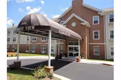 Front entrance of a brick senior living building with a covered driveway canopy and a clear blue sky.