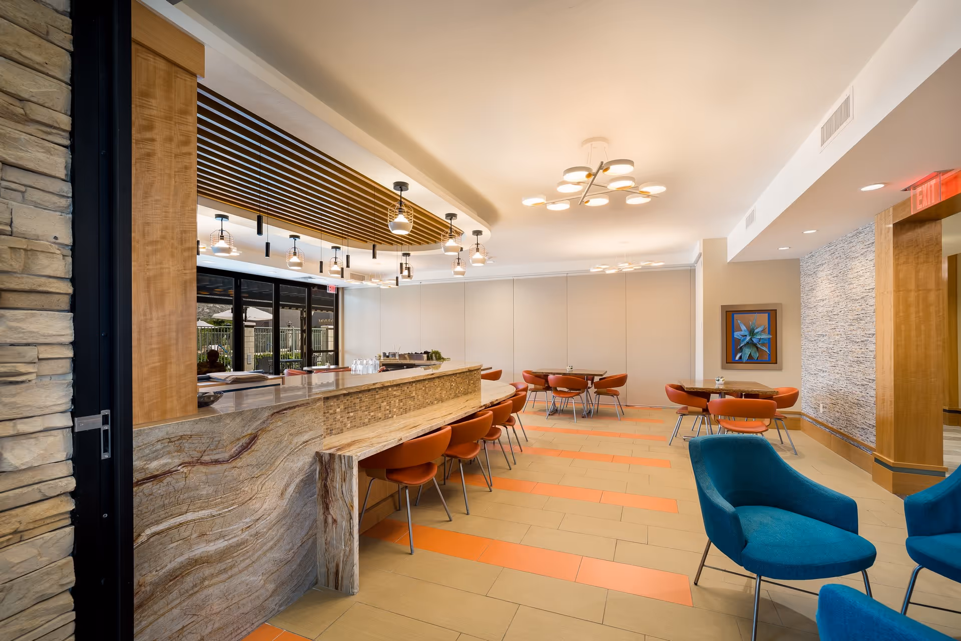 Well-lit modern dining/lounge area with a stone-topped bar, round tables and orange chairs.