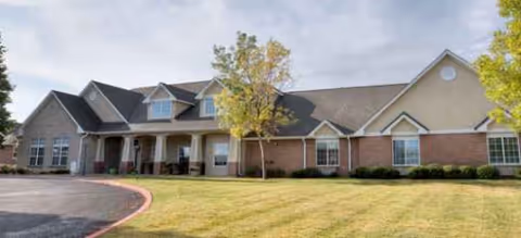 Exterior view of a single-story brick senior living facility with a curved driveway and lawn.