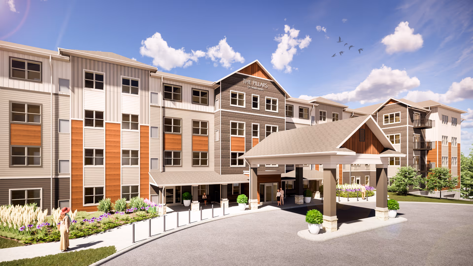 Front exterior of The Pillars of Grand Rapids senior living building with a covered drop-off entrance, landscaping and a few people.