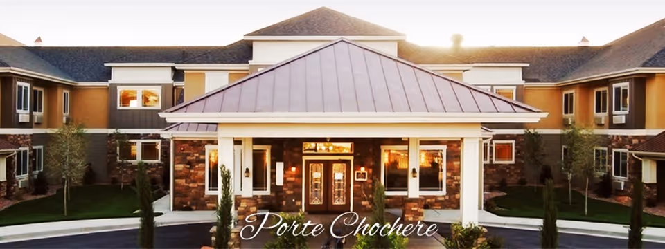 Front exterior of a two-story senior living building featuring a covered porte-cochere entrance with stone accents.