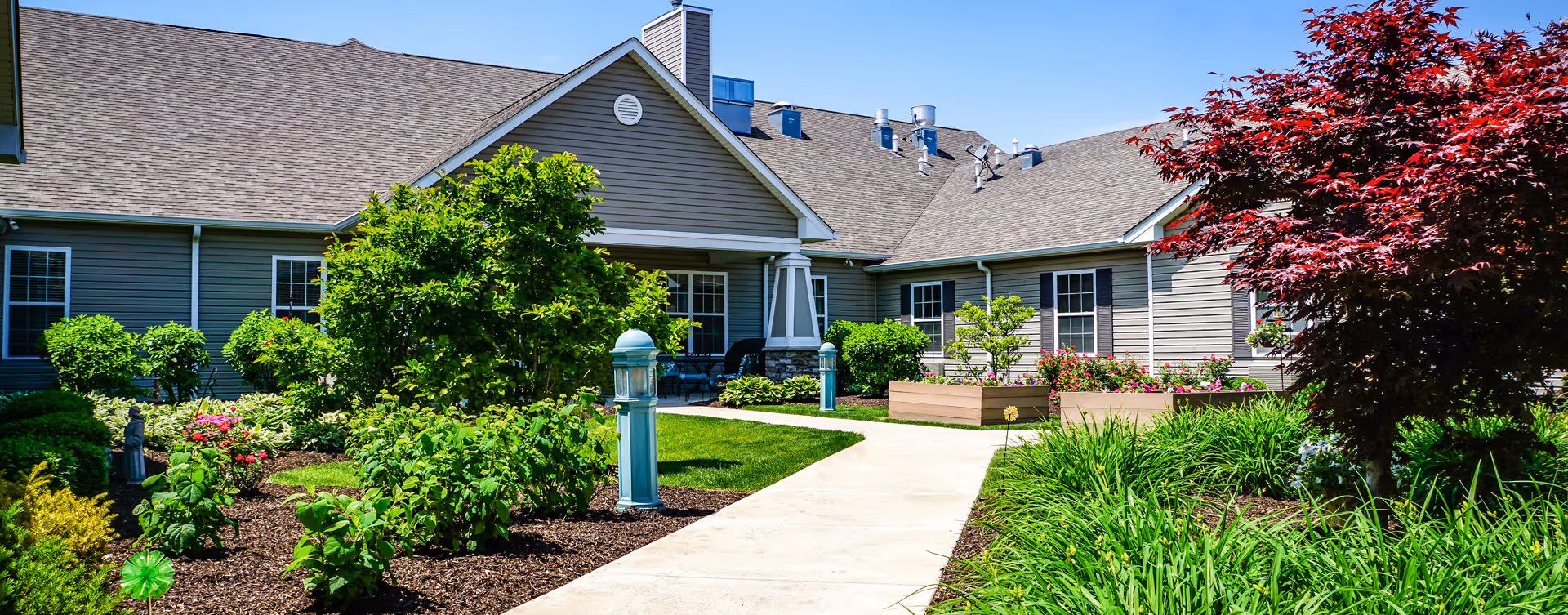 Landscaped courtyard with a paved walkway, raised planters, and shrubs in front of a single-story residential building.