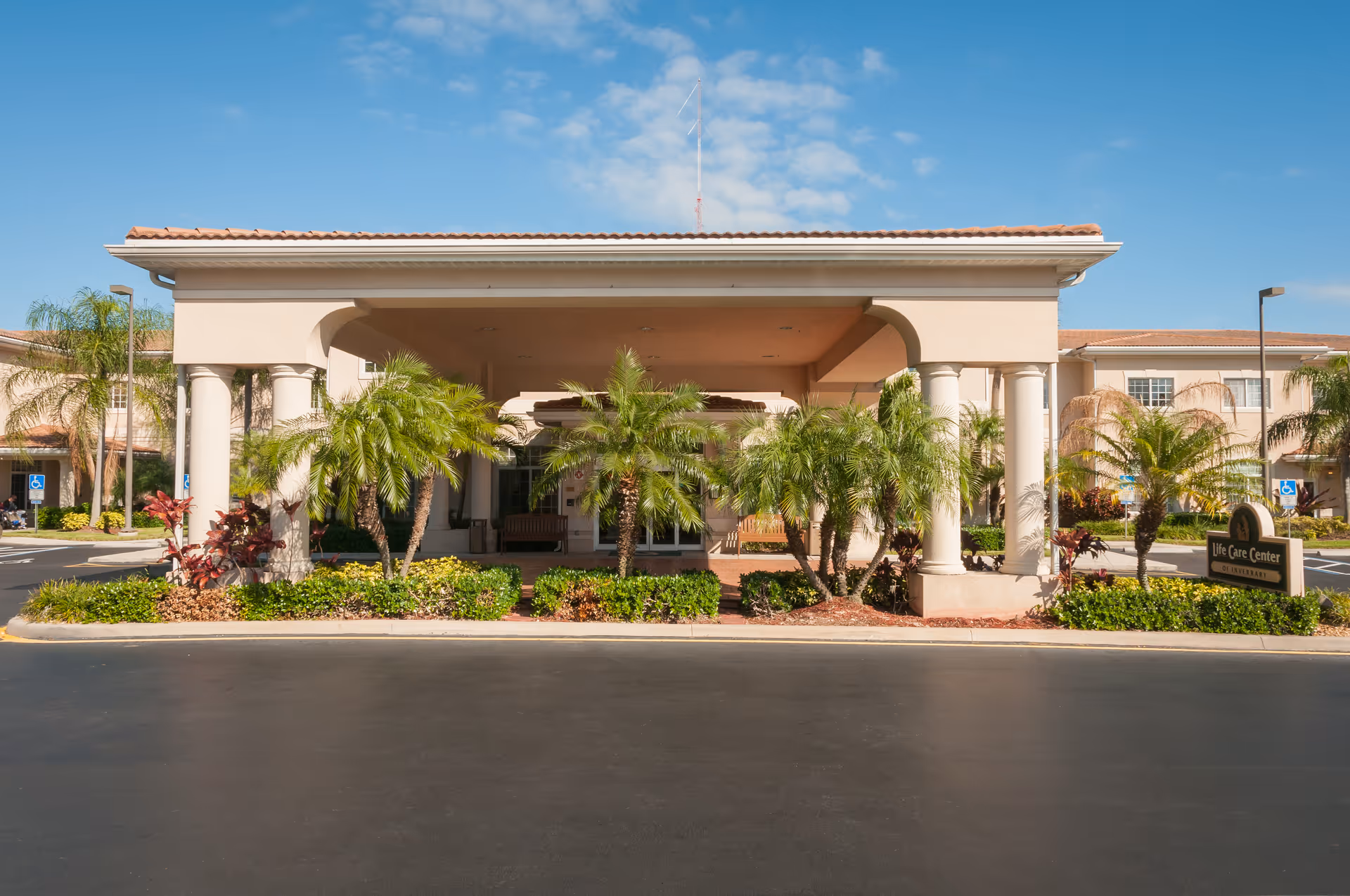 Front entrance of the Life Care Center building with a covered portico, columns, palm landscaping and a driveway.