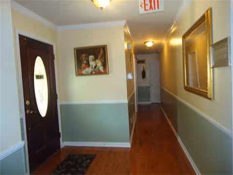 Interior hallway in a senior living facility with a door, framed art, and an exit sign.