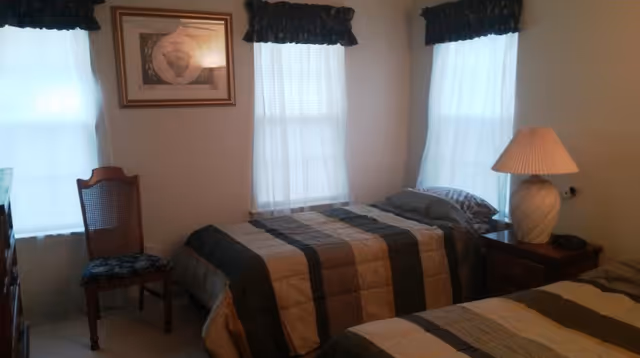 Two twin beds with striped quilts, a nightstand with lamp, and a chair in a bedroom.